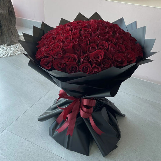 Bouquet of red roses wrapped in black paper with a red ribbon on a light gray floor.